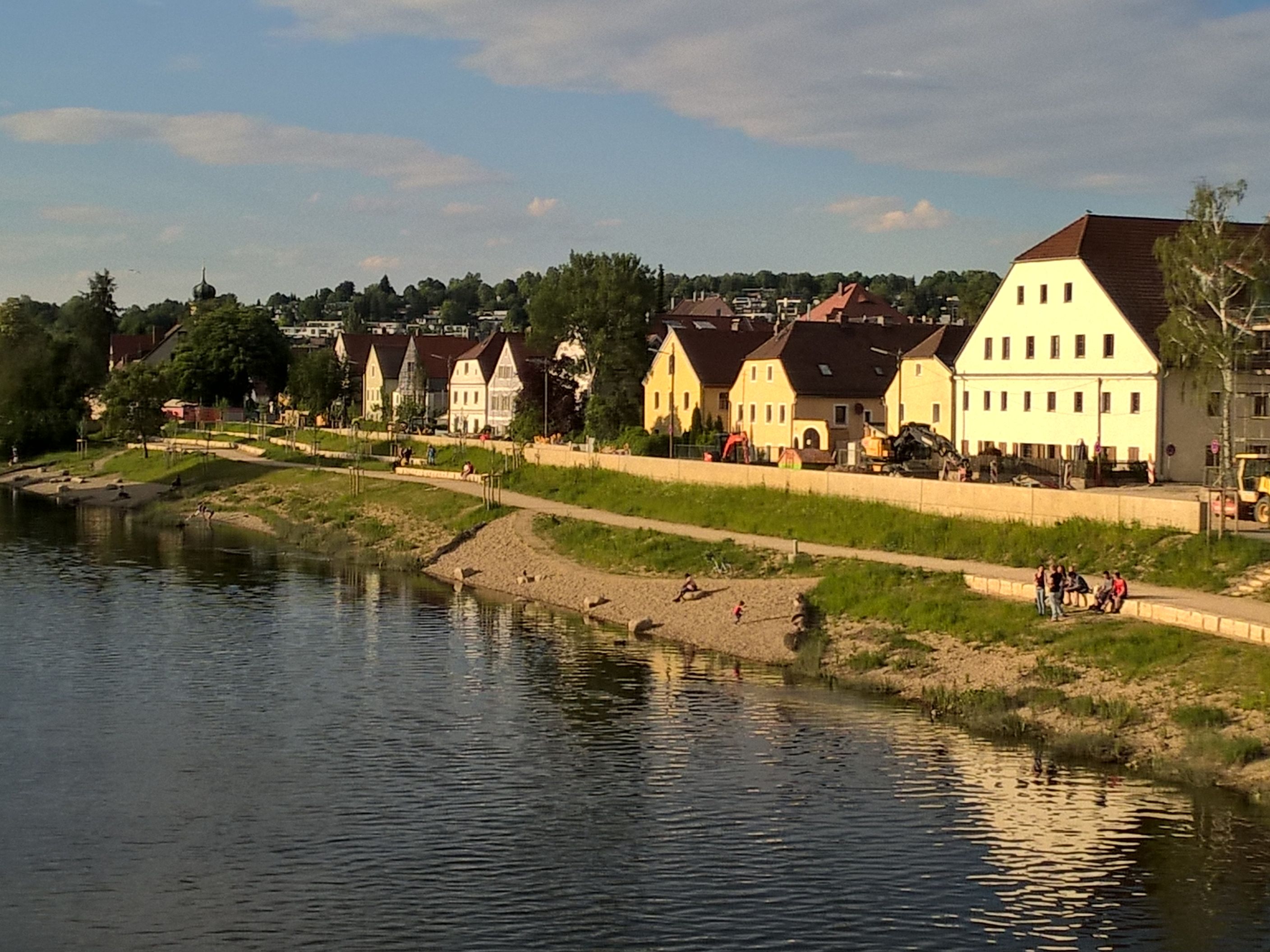 Der Fluß Regen im Vordergrund, daneben die neu angelegte Böschung mit Badebuchten und Natursteinreihen, dahinter die Hochwasserschutzmauer, die Obere Regenstraße mit einigen Baufahrzeugen und die Häuserreihe in der Oberen Regenstraße