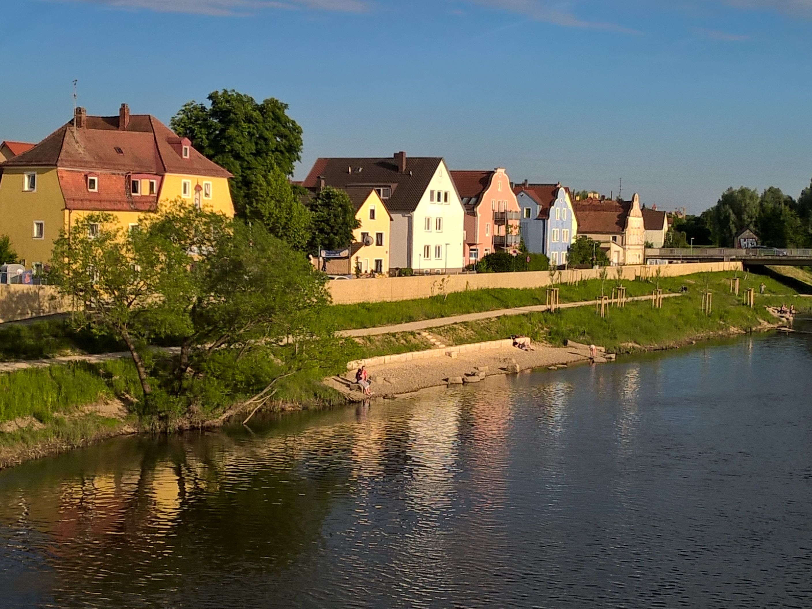 Der Fluß Regen im Vordergrund, die Böschung mit Badebucht und die Hochwasserschutzmauer, dahinter die bunte Häuserreihe in der Unteren Regenstraße