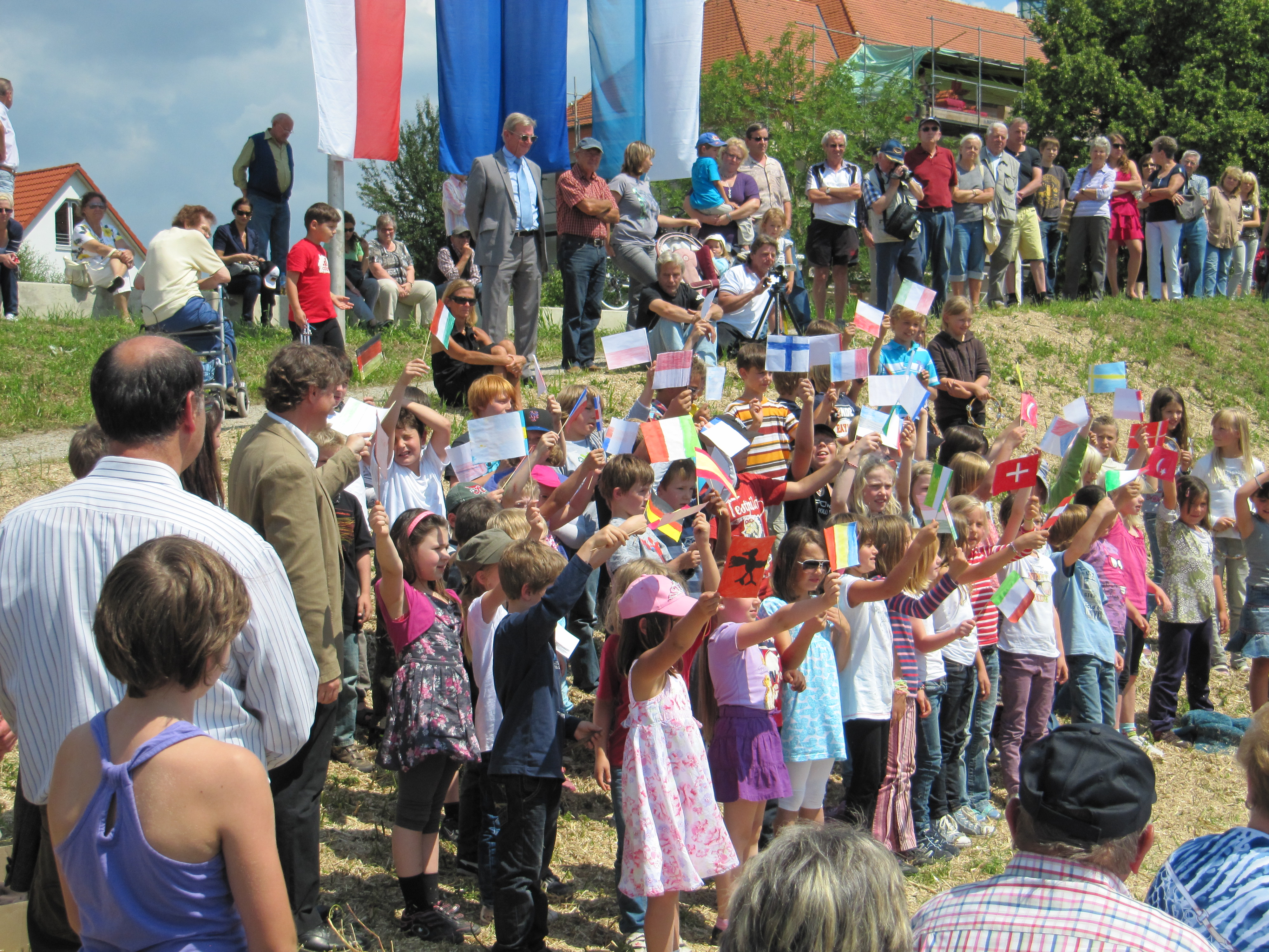 Im Vordergrund an der Deichböschung, die Kinder der Grundschule Schwabelweis winken mit bunten Fähnchen. Oberhalb der Böschung, auf der Deichkrone weitere Besucher der Einweihung