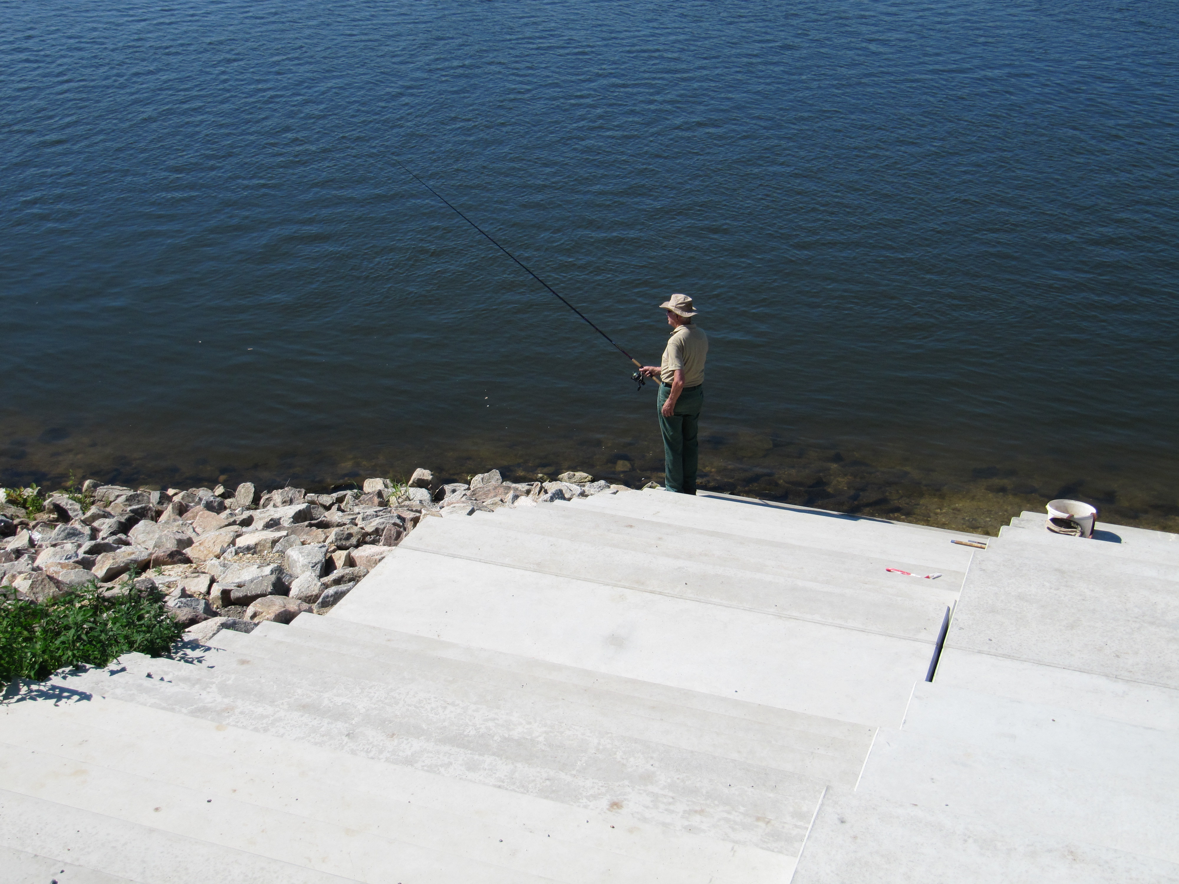 Die betonierte Treppenanlage hinunterschauend zur Donau, auf der letzten Stufe steht ein Angler