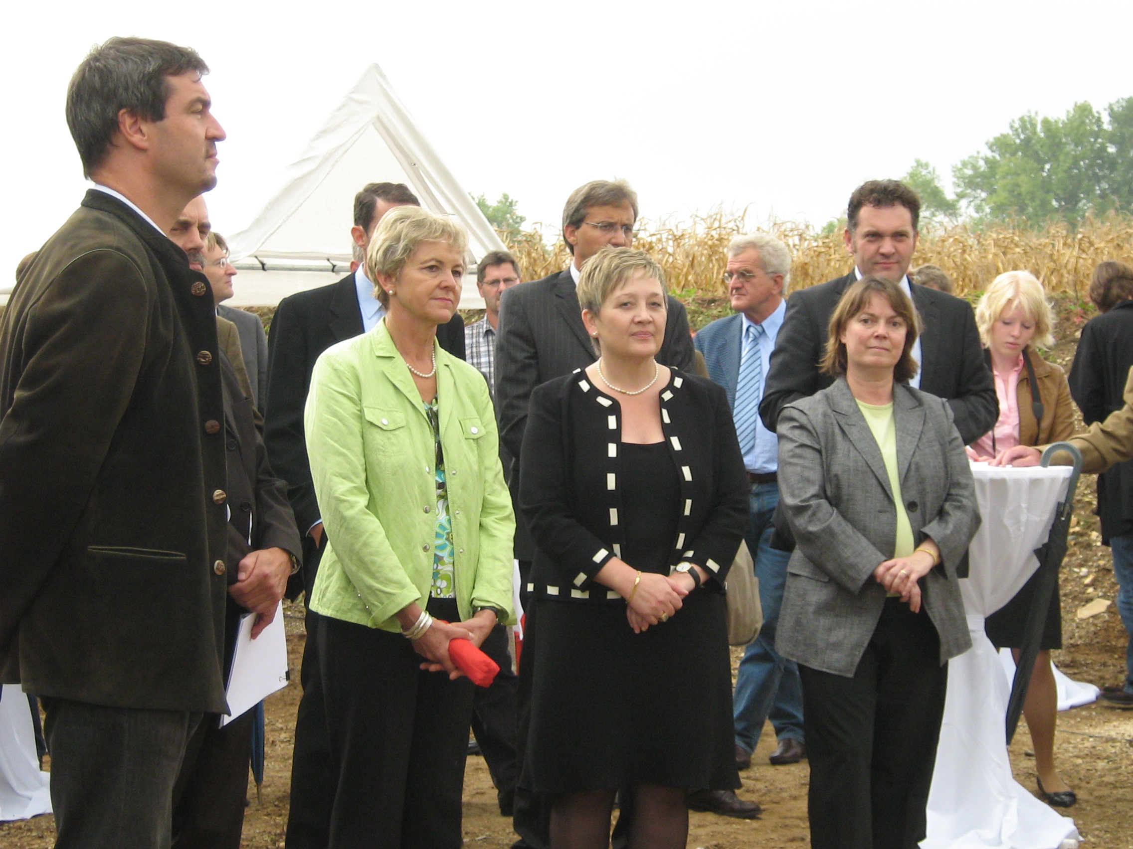 Umweltminister Markus Söder links im Bild mit mehreren Kommunalpolitikern. Im Hintergrund ist die Spitze des Pavillons und ein Maisfeld zu sehen.