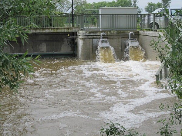 Beim Hochwasser im Juni 2013 war das Schöpfwerk in Betrieb. Quer im Bild das Schöpfwerk mit geschlossener Schütztafel, rechts wird aus den Rohrschächten Wasser aus dem Aubach gepumpt. Im Vordergrund die Wasserfläche, entlang des Übergangs führt ein grünes Geländer. Ein Schaltschrank steht rechts oberhalb der Rohrschächte und weiter rechts ein Fahrzeug.