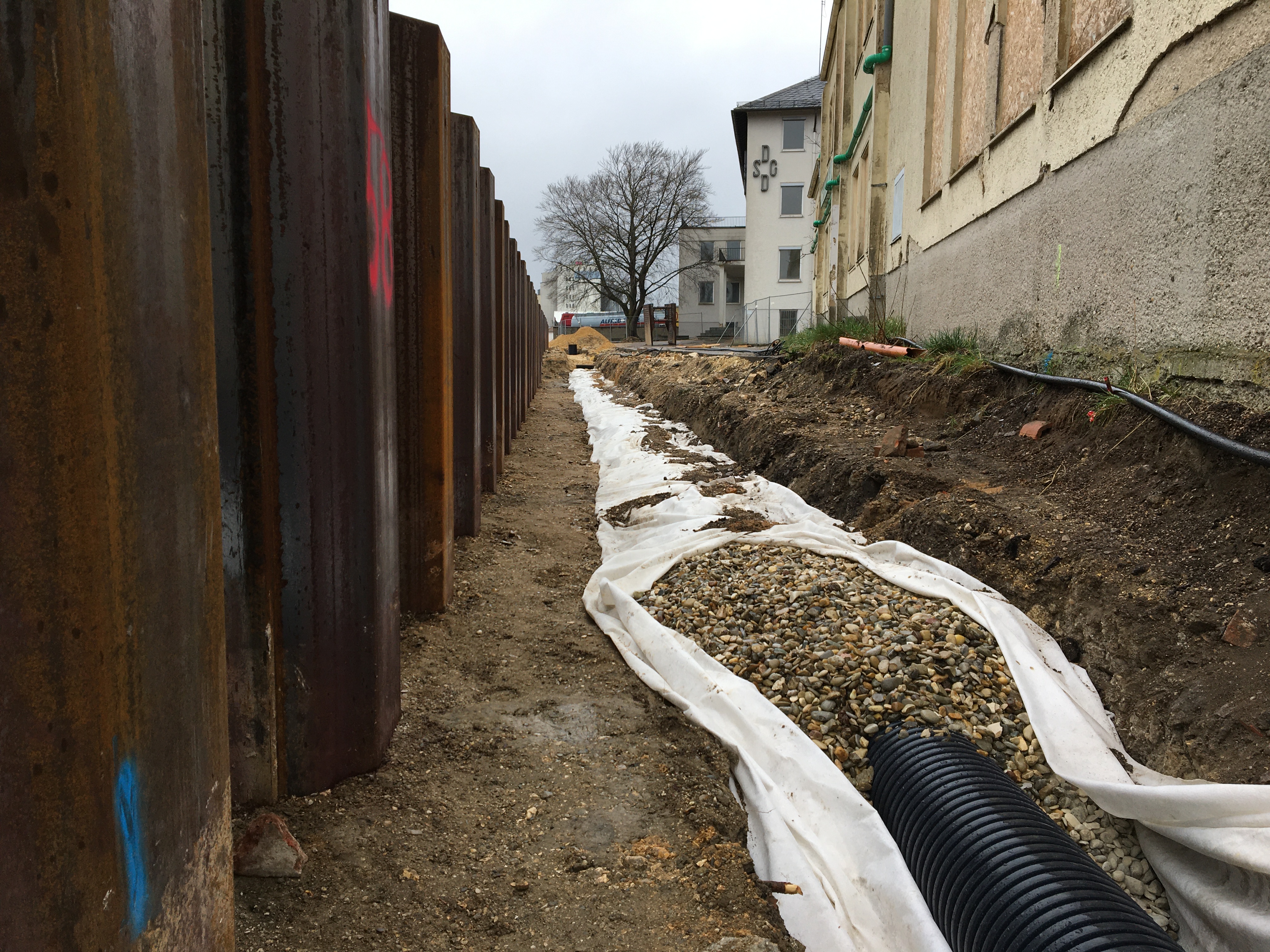 Links nach hinten verlaufend die Spundwand, rechts daneben der Filterkies mit Vlies ummantelt und Bebauung.