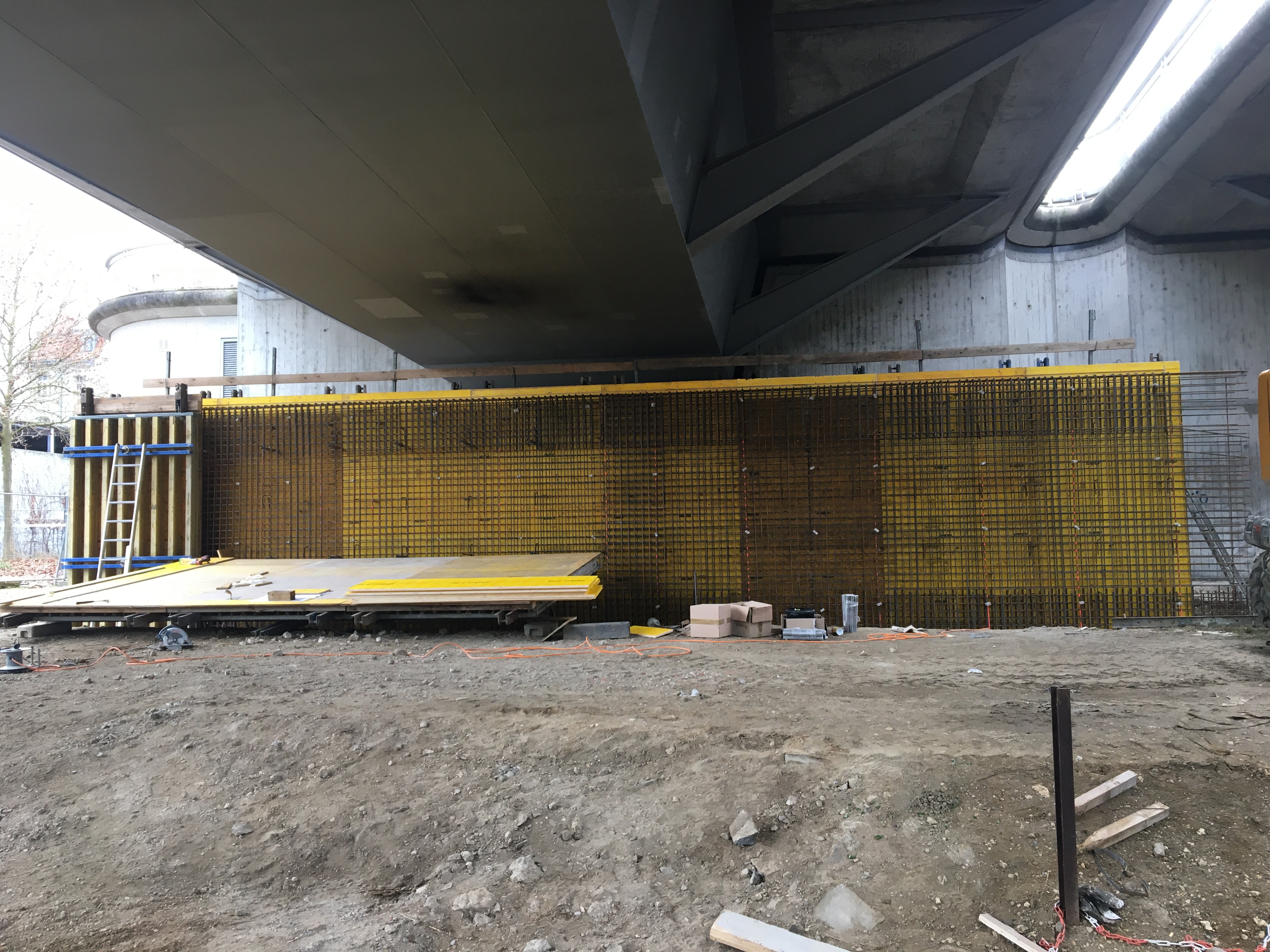 Gelbe Schalbretter mit Bewehrungsstahl unter der Nibelungenbrücke, im Vordergrund die Baustraße mit Werkzeug