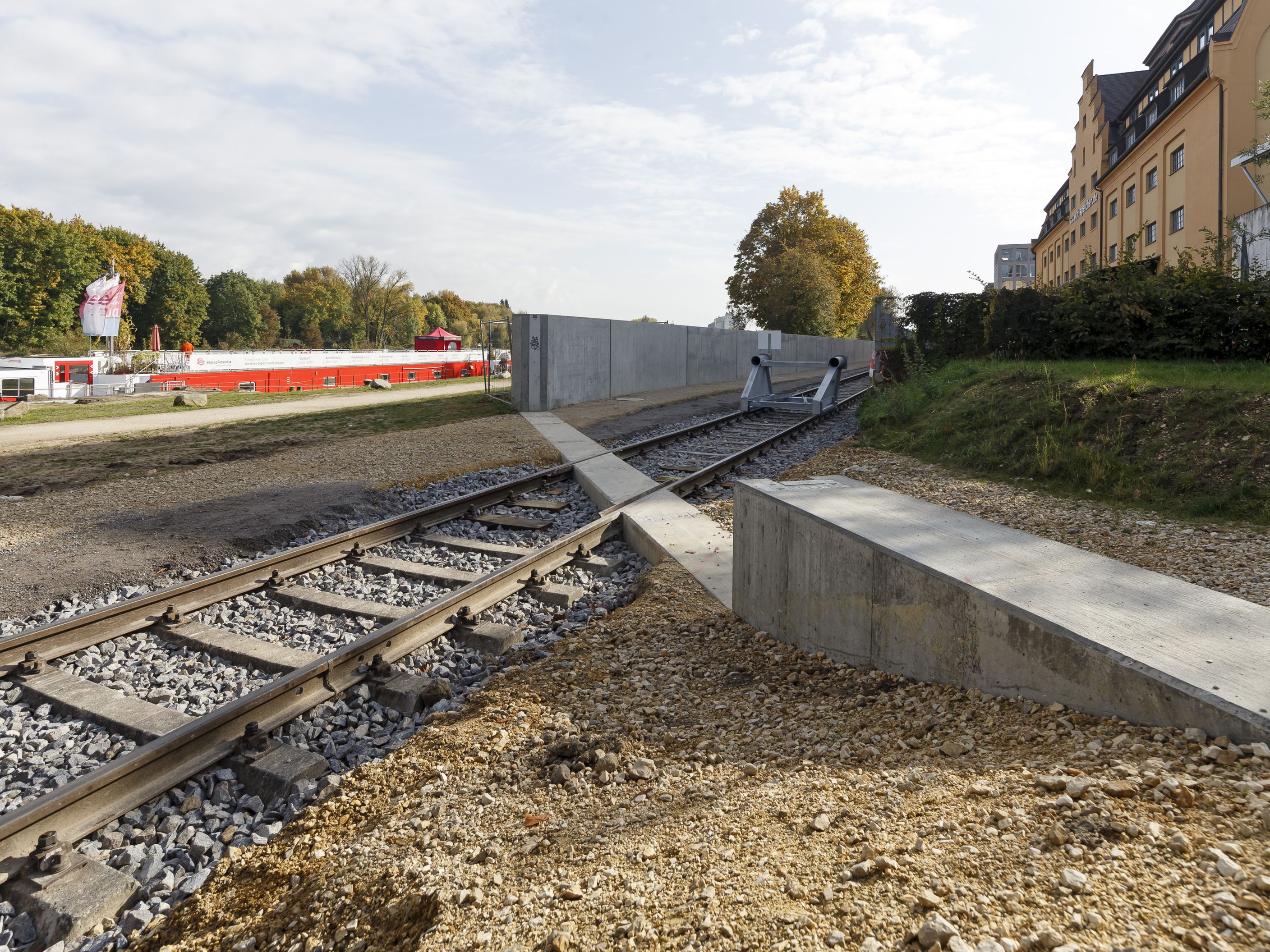 Diagonal im Bild verlaufen Gleise. Auf beiden Seiten endet die Hochwasserschutzwand. Diese Lücke muss im Hochwasserfall mit mobilen Elementen verschlossen werden. Rechts steht der IT Speicher, links am Donauufer ist das Oberdeck eines Flussschiffes zu erkennen.