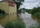 überflutete Straße, links Häuser die im Wasser stehen, rechts Büsche