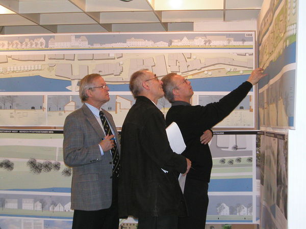 Drei Mitarbeiter betrachten in einem Ausstellungsraum die Pläne vom Hochwasserschutz