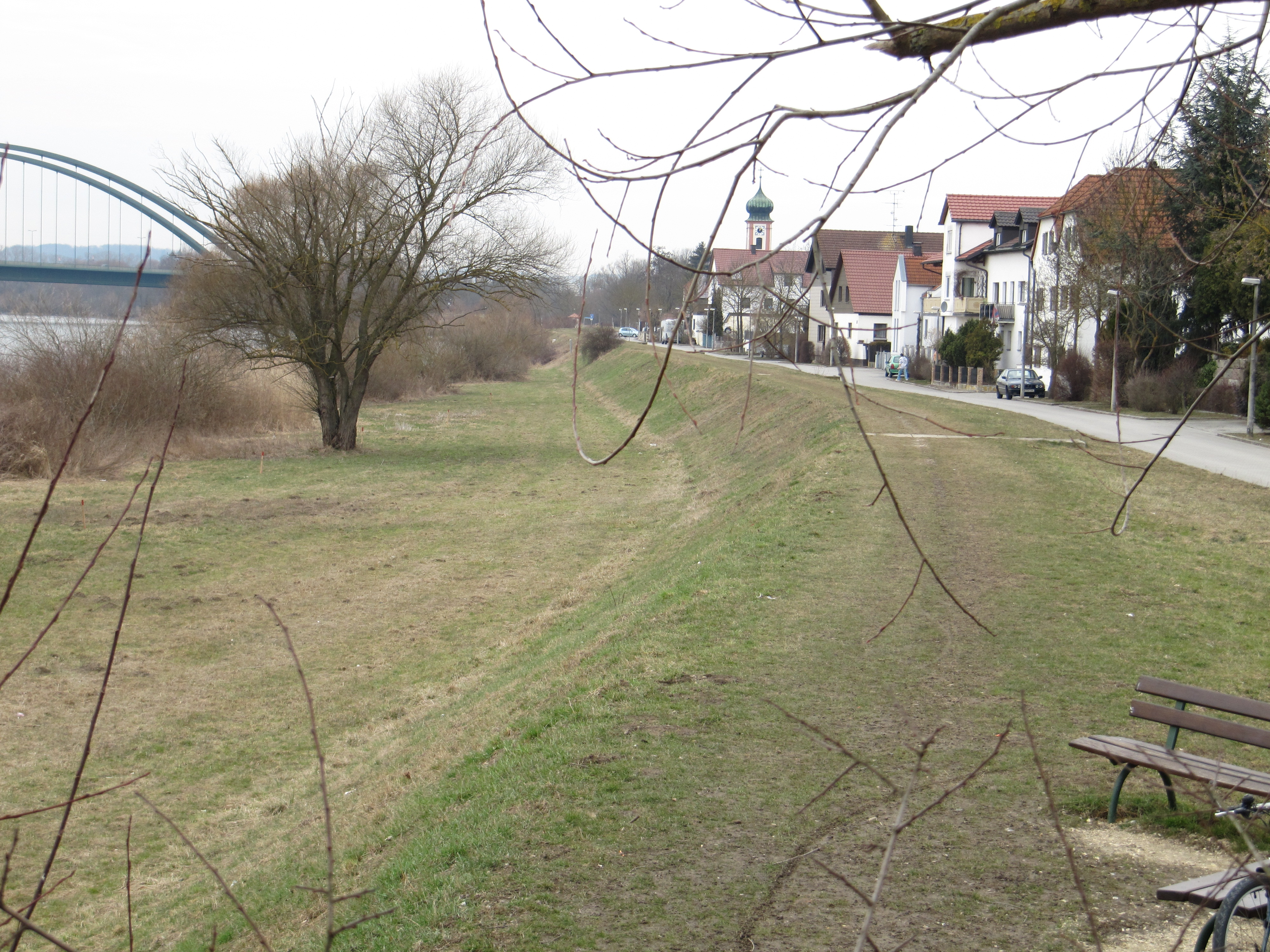 vorhandener Damm Ein grüner Damm mit einer Brücke im Hintergrund.