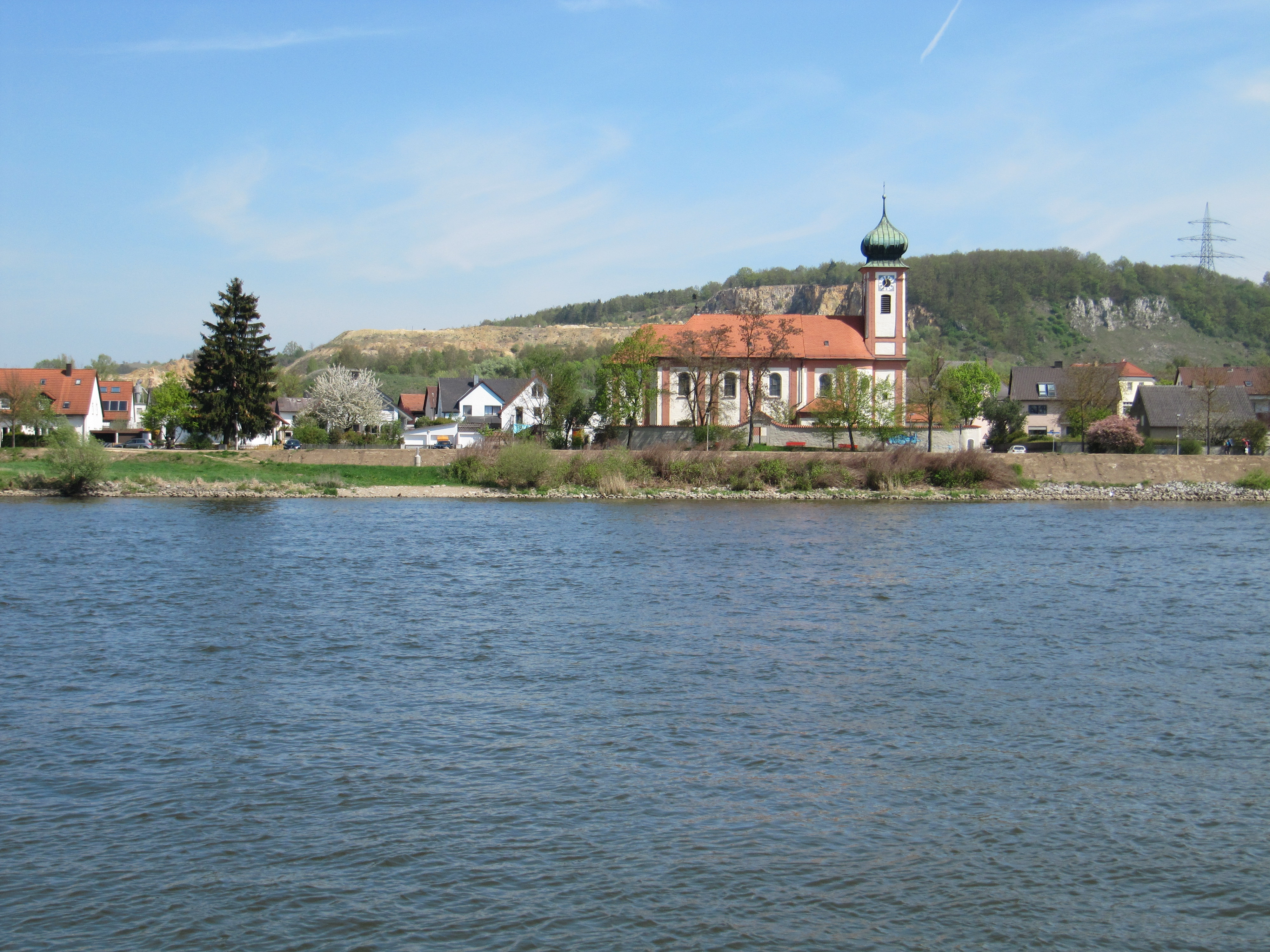 Schwabelweis Donau mit Uferstreifen . Nahe am Ufer gebaute Häuser und die Kirche.