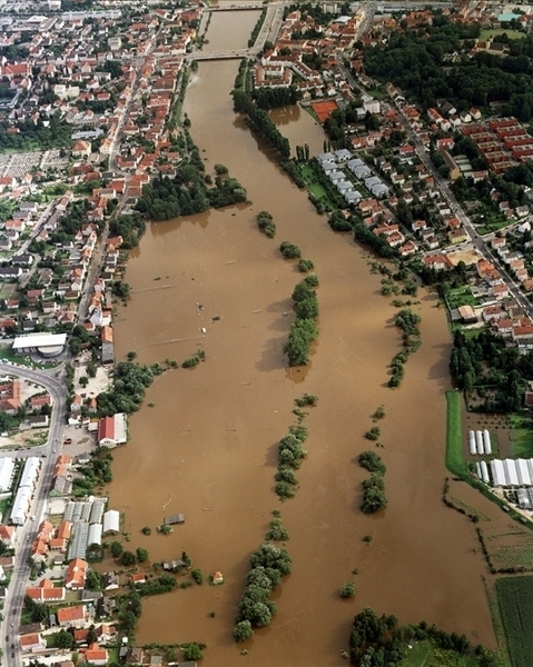 Ein Luftbild von der Stadt mit großen überschwemmten Flächen. Die Donau hat sich auf beide Seiten ausgebreitet und die Flächen mit braunen Wasser bedeckt.