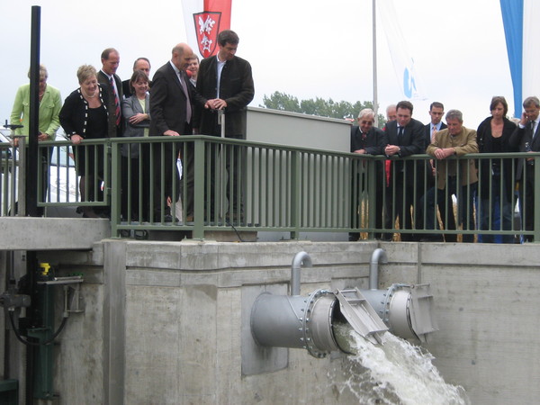 Umweltminister Söder und Oberbürgermeister Hans Schaidinger stehen auf einem Damm und drücken auf einen weißen Knopf, der die Schleuse öffnet. Darunter schießt das Wasser aus dem Schleusenrohr.