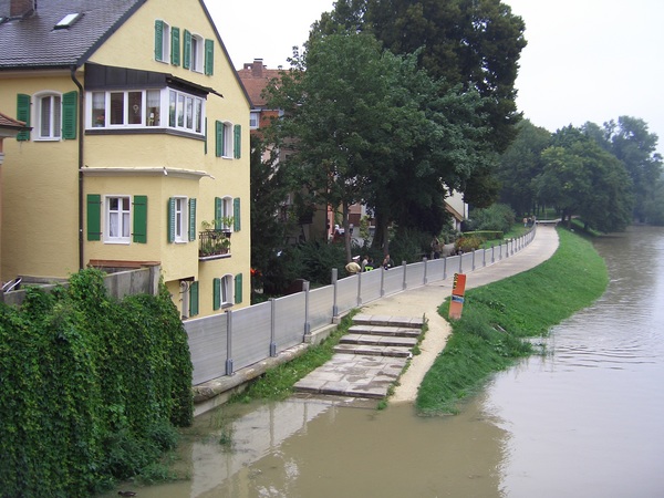 Vor einem Haus sind die Hochwasserwände aneinander gereiht. Die Donau ist rechts davon und hoch.