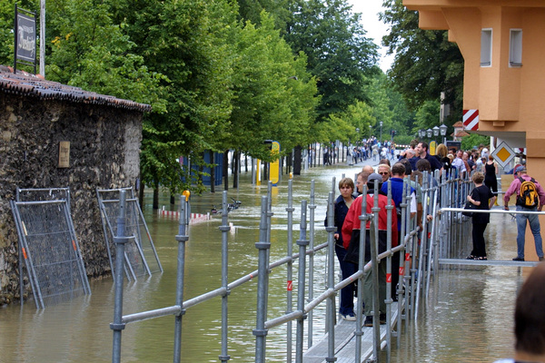 Menschen laufen auf aufgebauten Fußgängerstegen auf einer, vom Hochwasser, überfluteten Straßen